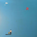 A man and child watching a small red plane in a blue sky