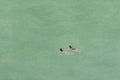Two tiny swimmers in a vast jade-green sea