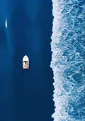 A small white boat on deep blue water beside a line of surf, seen from above