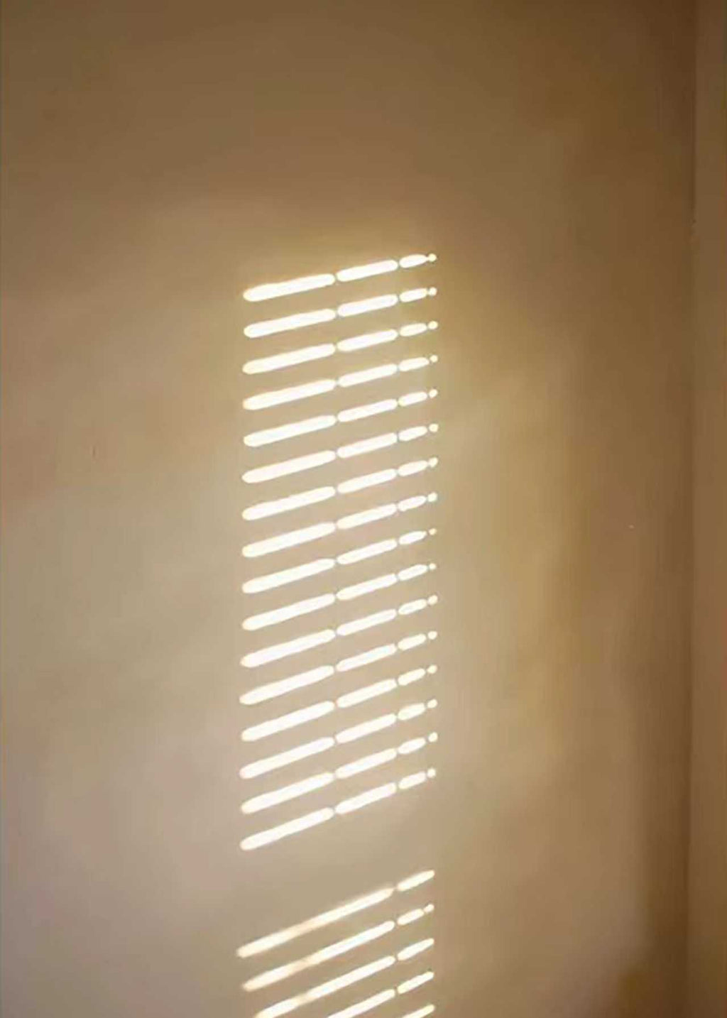 Narrow bars of sunlight on a warm beige wall