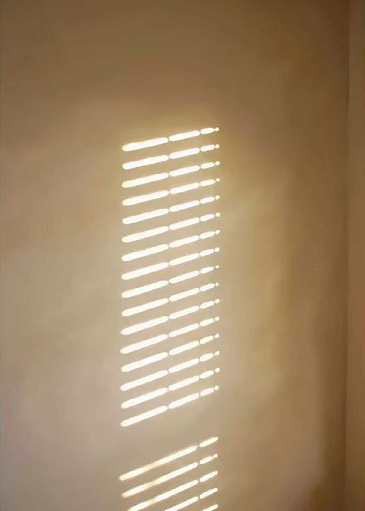 Narrow bars of sunlight on a warm beige wall