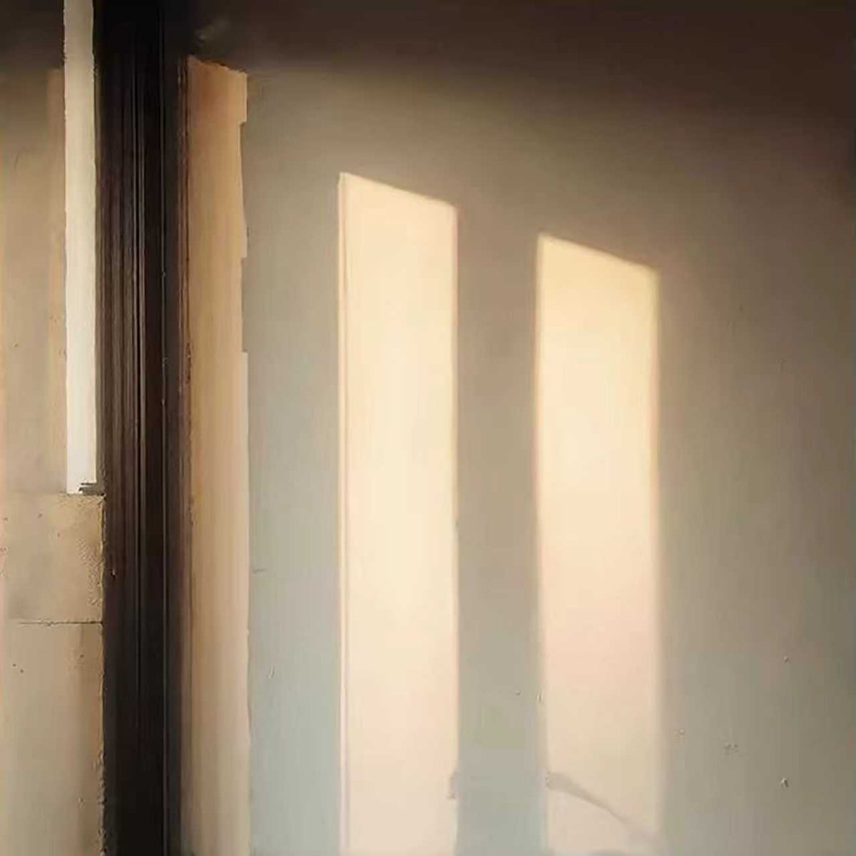 Two shafts of warm light falling on a dim wall by a window