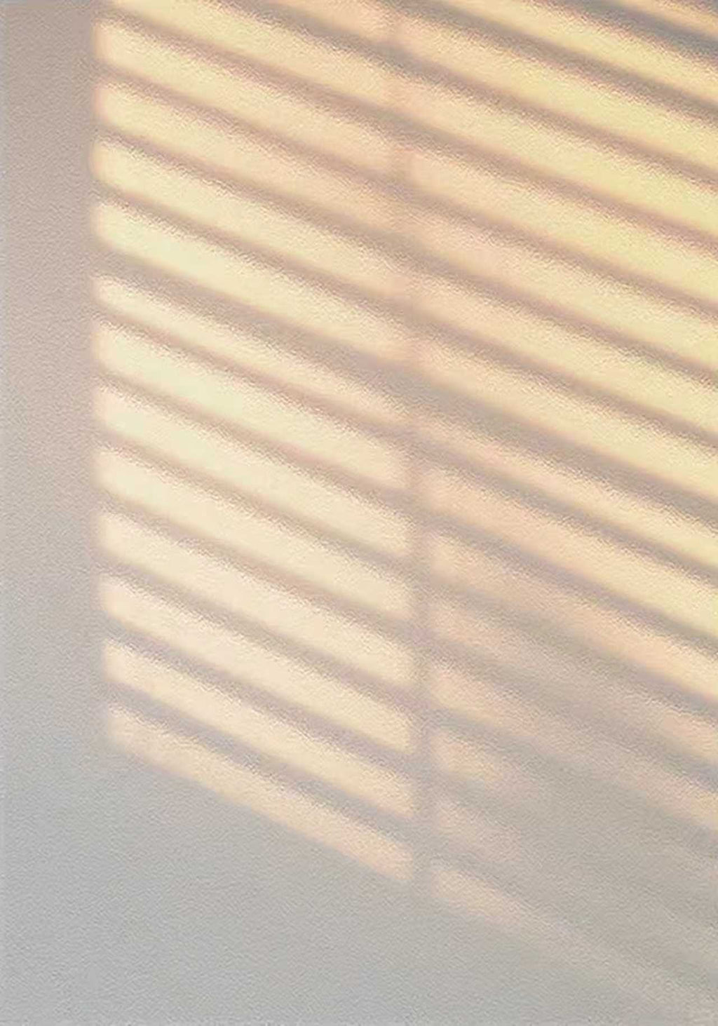 Striped light from a window blind on a pale wall