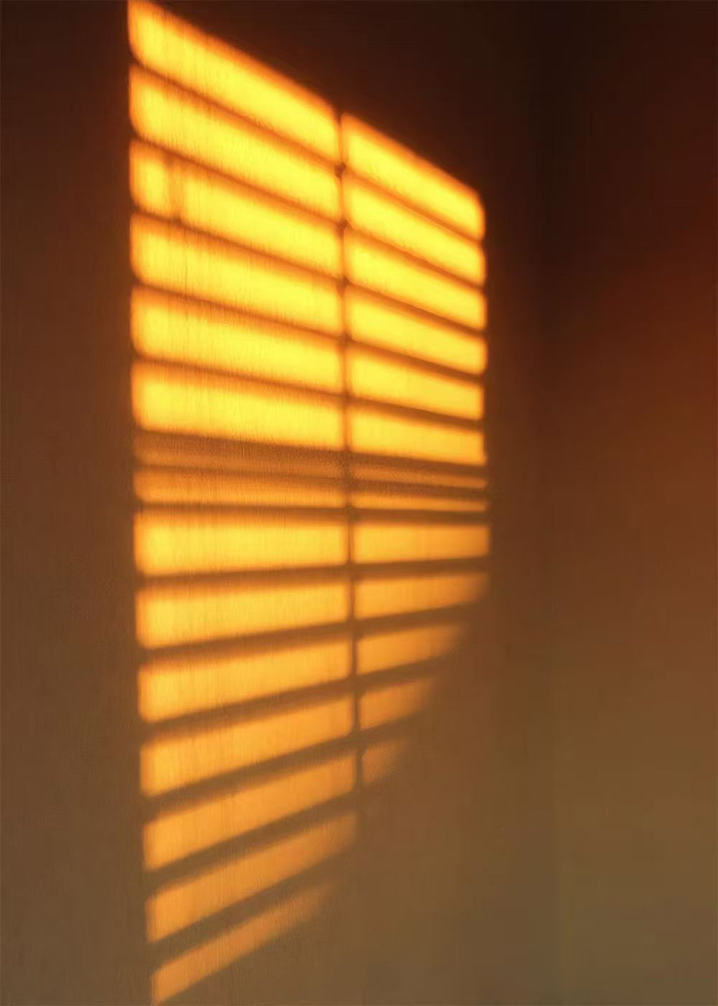 Bright amber stripes of light from a blind on a dark wall