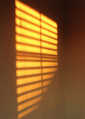 Bright amber stripes of light from a blind on a dark wall