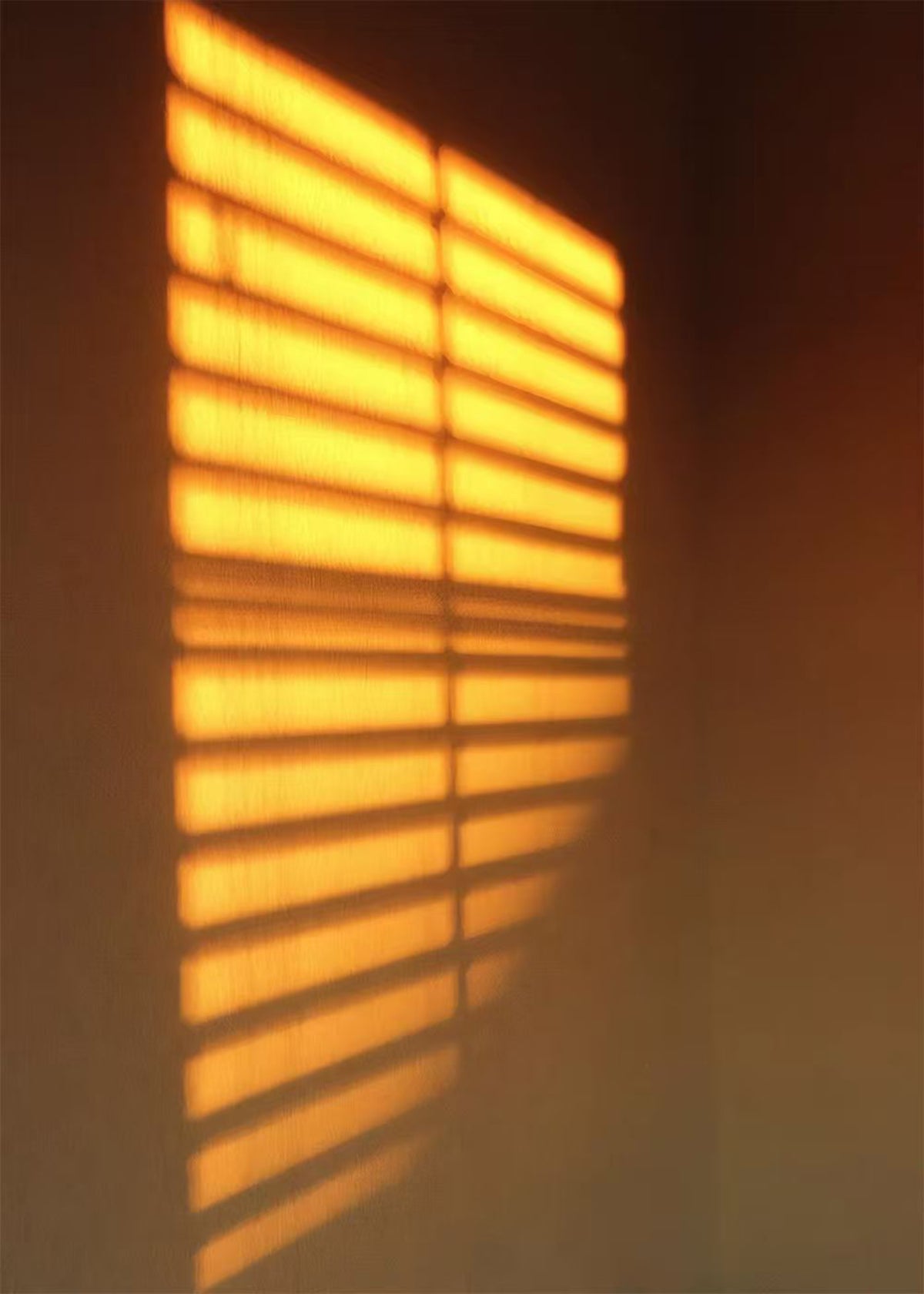 Bright amber stripes of light from a blind on a dark wall