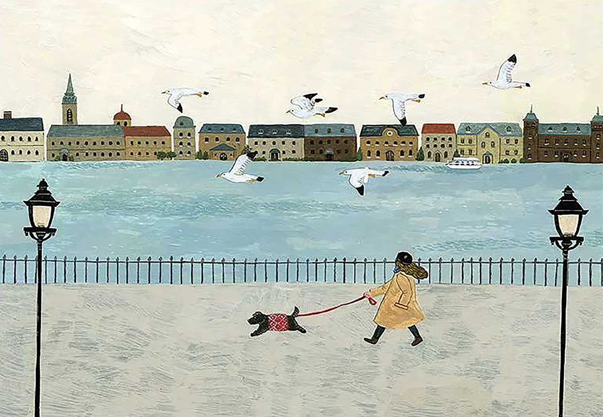 A figure in a yellow coat walking a little black dog along a riverside promenade with gulls and a town beyond