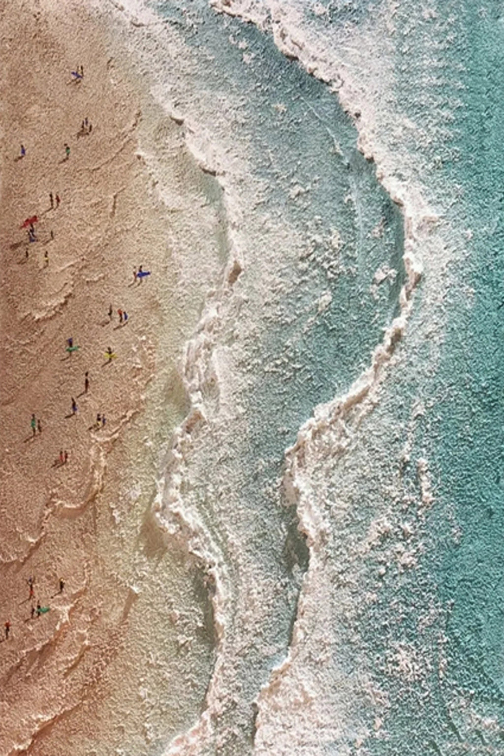 Tiny figures along a winding white tide line between sand and teal water