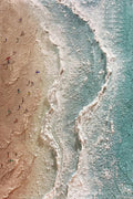 Tiny figures along a winding white tide line between sand and teal water