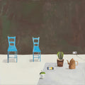 Two blue wooden chairs against a dark wall, a cactus, a teapot and odd objects on the pale floor