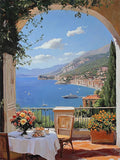 A shaded terrace table with flowers looking out over a blue bay, white villas and hills