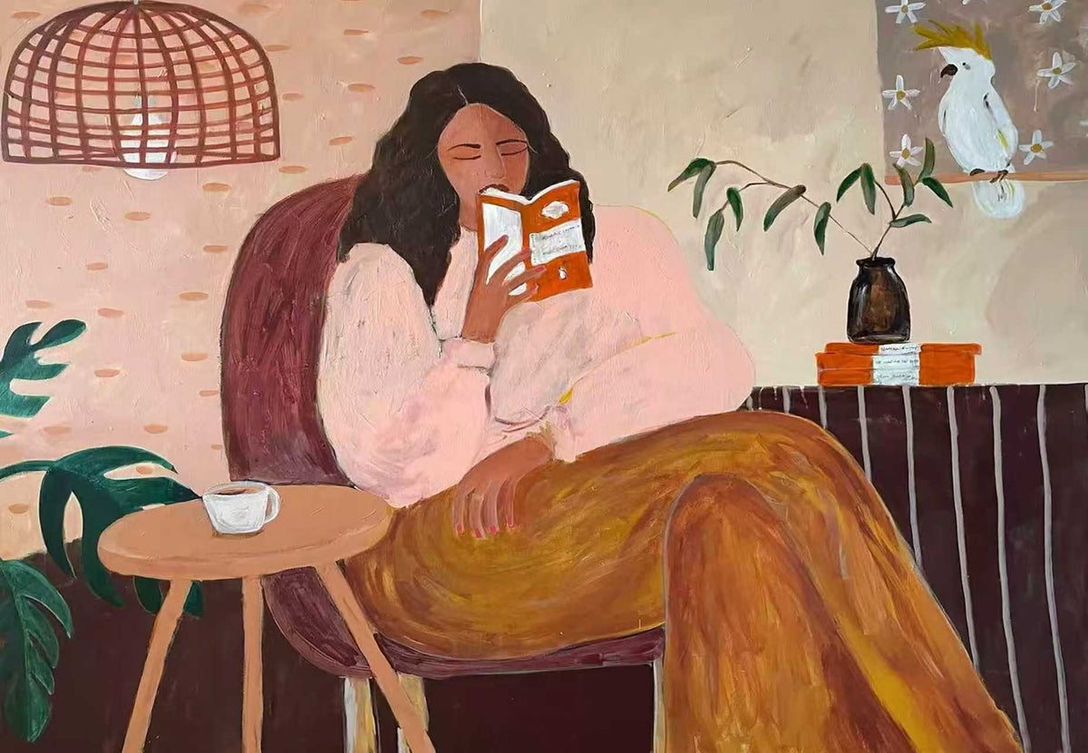 A woman curled up reading in an armchair beside a tea table, a white cockatoo perched behind her