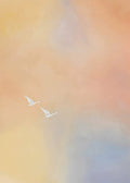 Two white swans flying through a soft haze of peach, gold and lilac