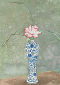 A single pink rose and a sweeping branch in a slender blue-and-white porcelain vase