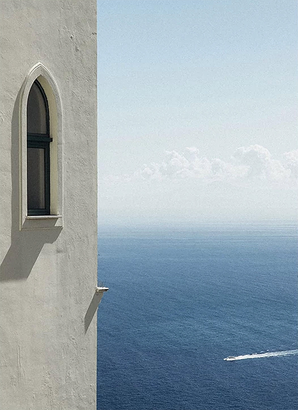 An arched window in a white wall above a deep blue sea, a single boat leaving a wake