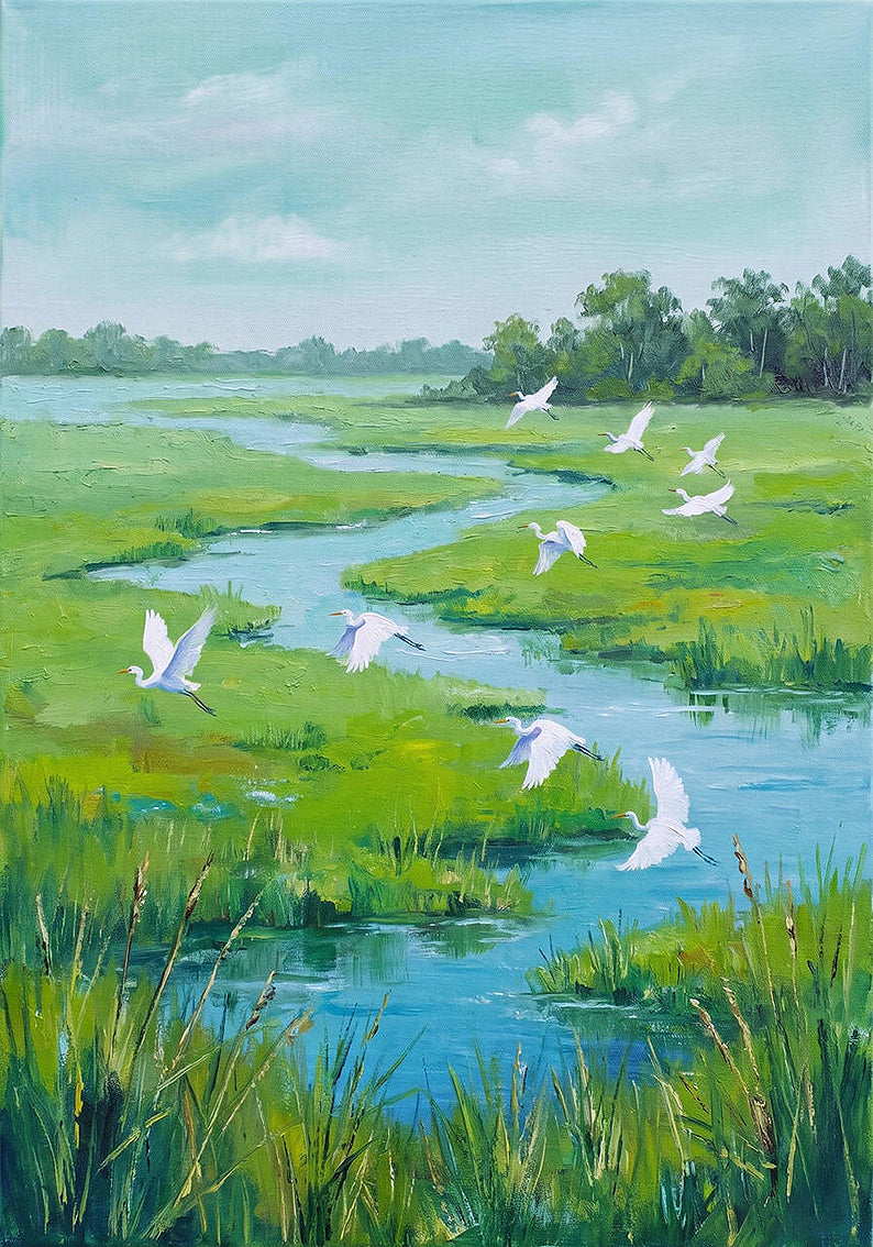 White egrets flying low over a winding blue creek through bright green marsh grass