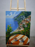 A café table overlooking a cliffside town above a bright blue sea.