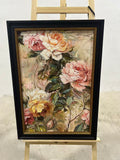 Blush and cream garden roses with lush green leaves in a dark frame.