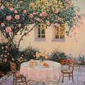 A lace-covered table set for tea beneath a blooming pink rose tree in a sunlit courtyard