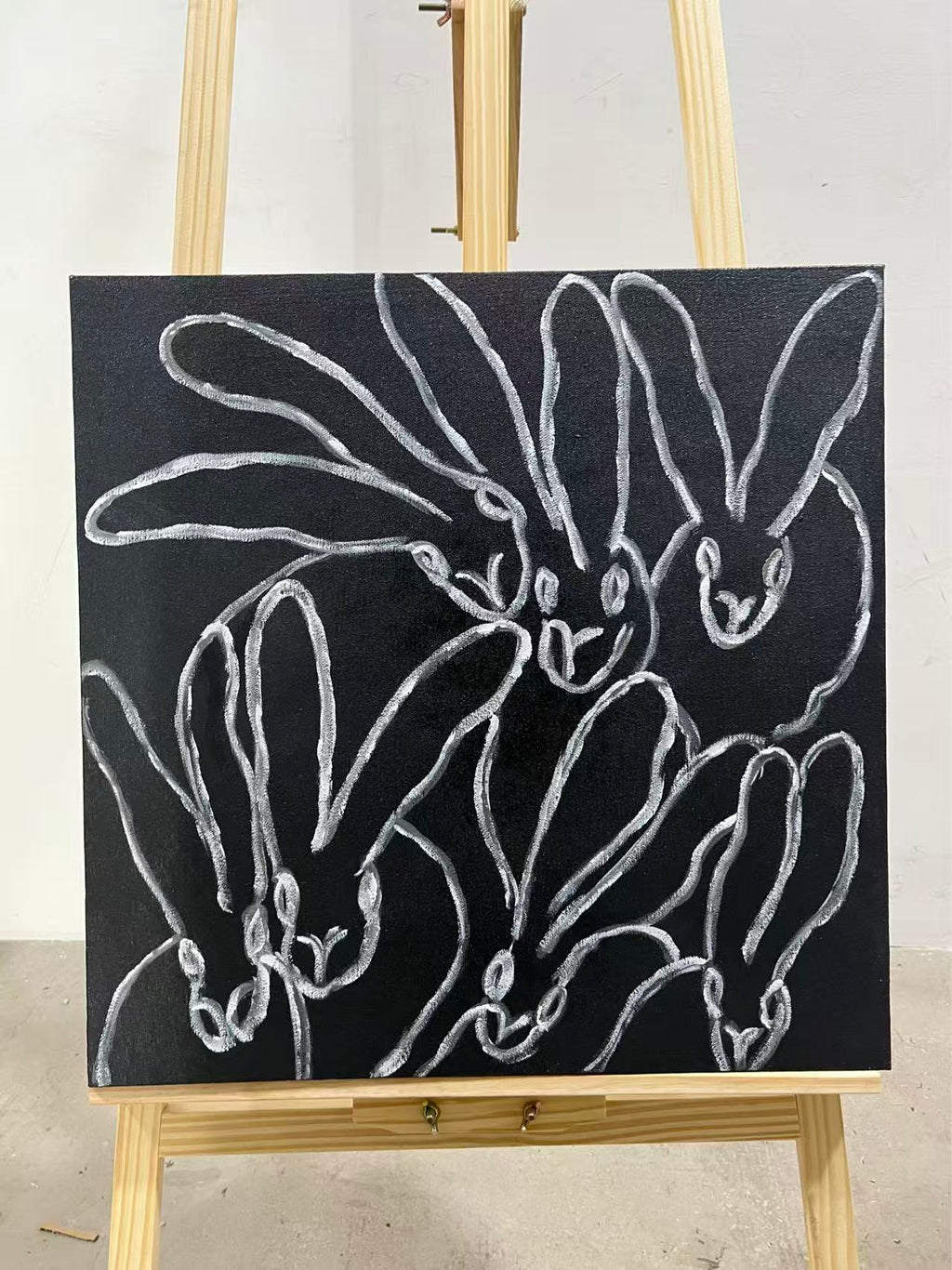 A white one-line drawing of a rabbit and reaching hands on a black ground.